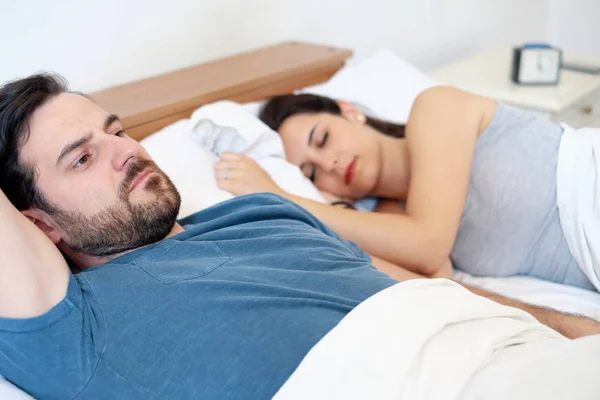 Depressed young man lying in bed and having problems with his girlfriend