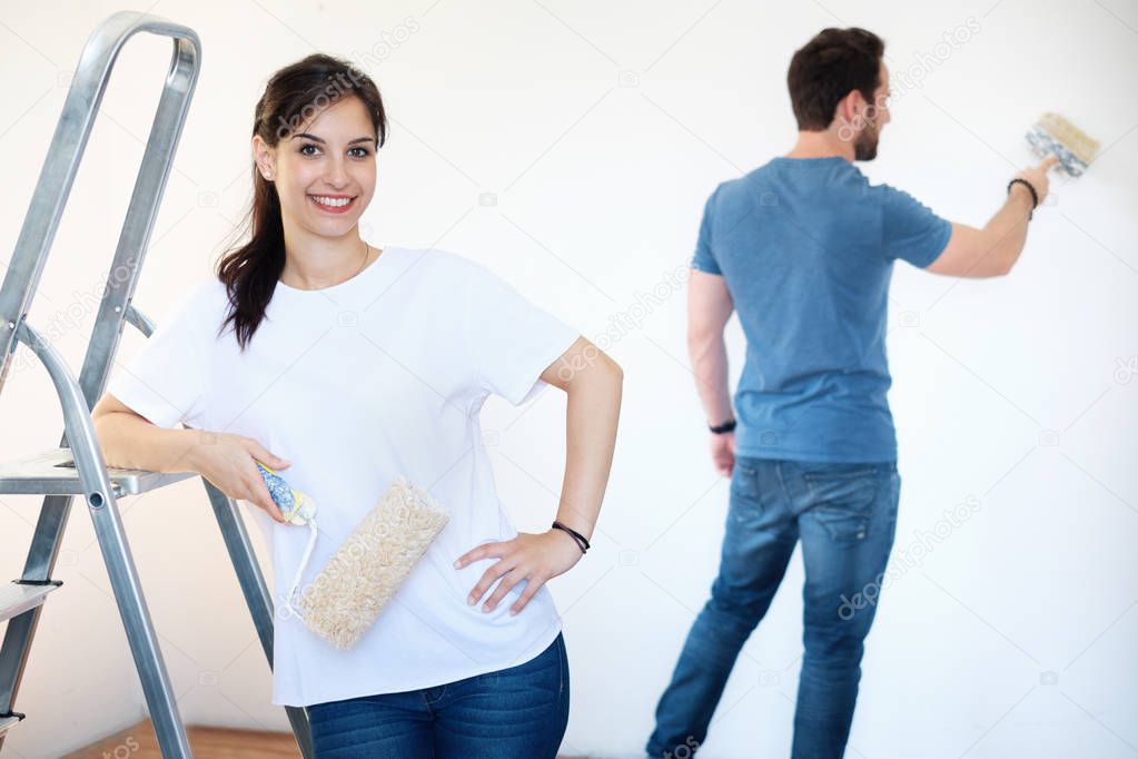 Young couple painting walls in their new house, do it yourself concept