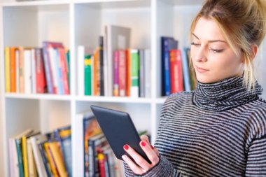 Genç kız e-kitap okuyucu renkli bookshelf yanındaki okuma