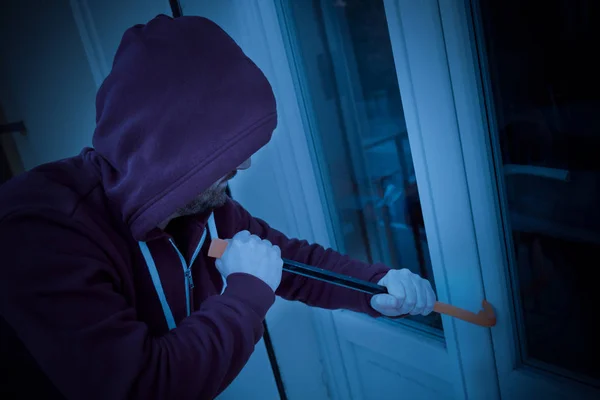戴着帽子的窃贼强迫窗户锁在晚上的房子里偷窃 — 图库照片