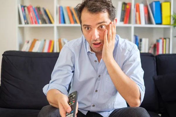 Shocked man watching television sitting on the sofa