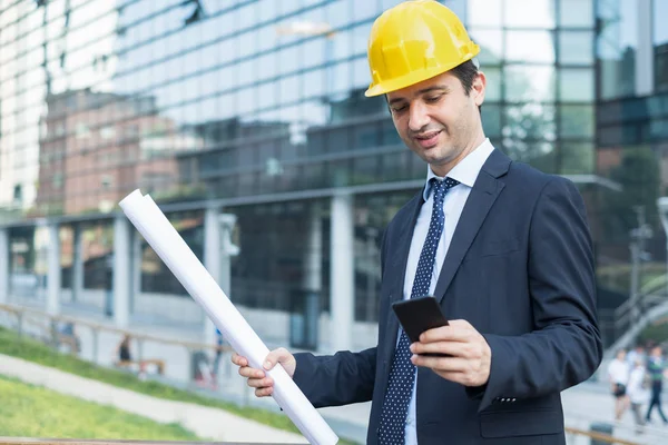 Businessman standing in suit on the construction site using smartphone app