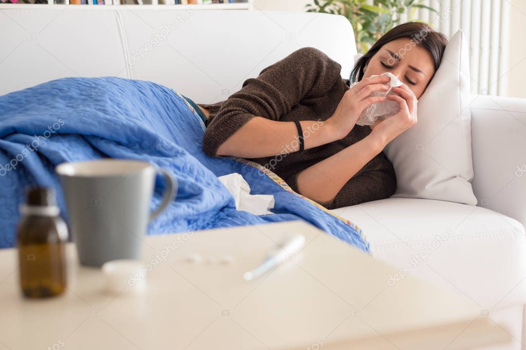Sick woman portrait sneezing her nose at home