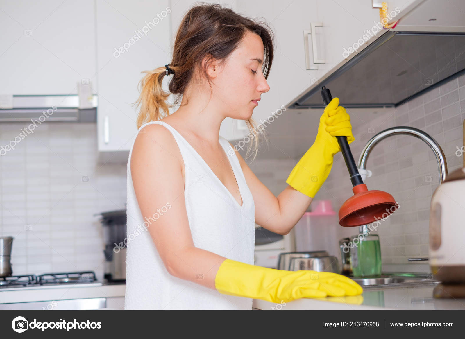 upset woman using plunger in blocked kitchen sink, Stock image