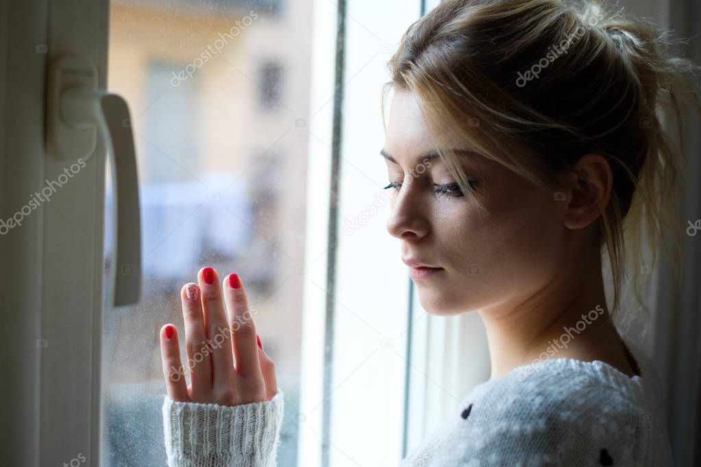 Beautiful sad girl by the window on a cold day