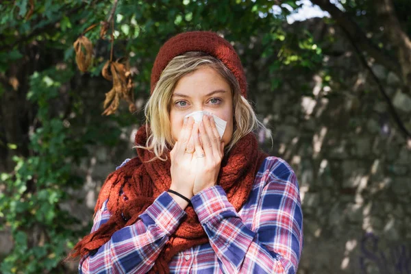 Girl feeling sick blowing nose outdoor in the park