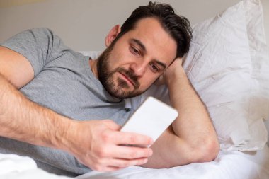 Cep telefonu tutan yatakta yatan rahat adam