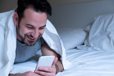 Cep telefonu tutan yatakta yatan rahat adam