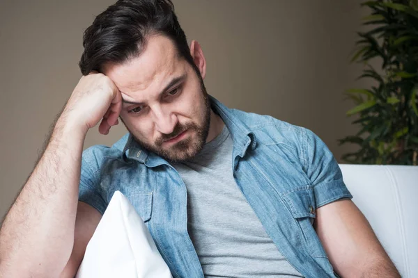 Man suffering and feeling alone at home sitting on the sofa