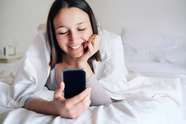 Young woman in bed watching smartphone