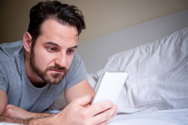 Neşeli adam izlerken cep telefonu ekran yatakta
