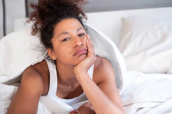 Black woman with sad expression lying in bed