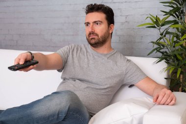 Adam kanepede evde oturmuş televizyon seyrediyor