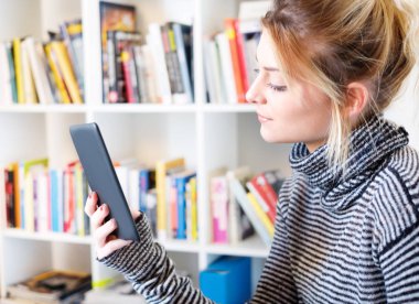 Genç kız e-kitap okuyucu renkli bookshelf yanındaki okuma