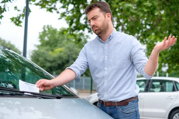 Angry man looking on parking ticket placed under windshield wiper