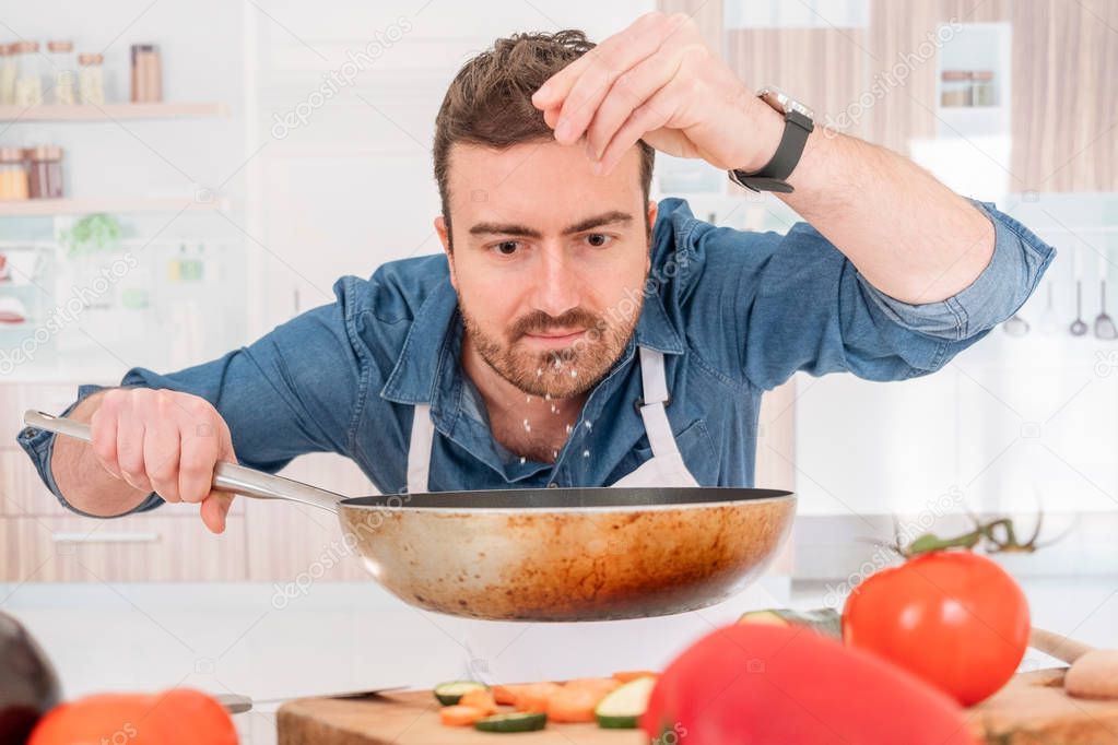 One man is cooking in his kitchen and adding salt