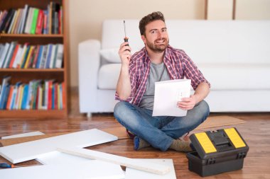 Mutlu genç adam mobilya montajı için yönergeleri okuma