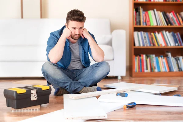 Trauriger junger Mann beim Lesen der Anleitung zum Zusammenbau von Möbeln — Stockfoto