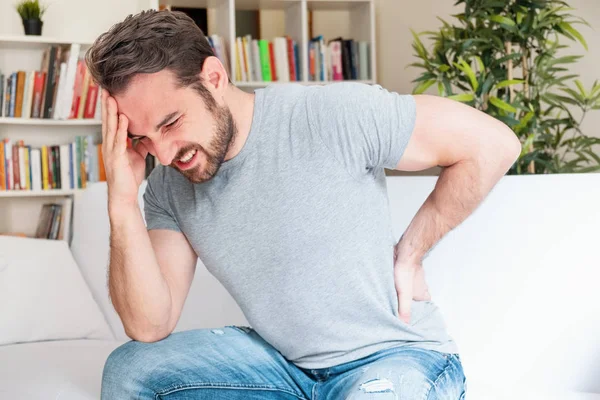 Un uomo che soffre di mal di schiena seduto sul divano a casa — Foto Stock