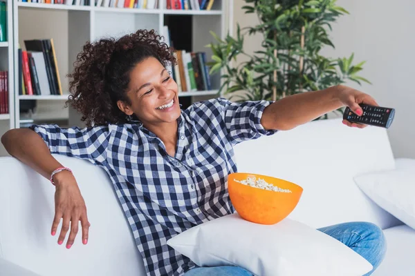 Чорна жінка дивиться телевізор вдома і тримає пульт дистанційного керування — стокове фото