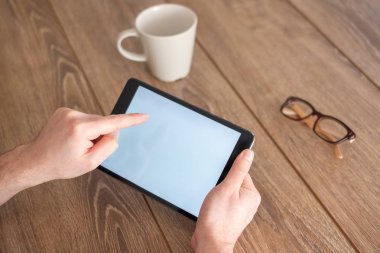 Elinde ahşap bir masa üzerinde dijital tablet tutarak