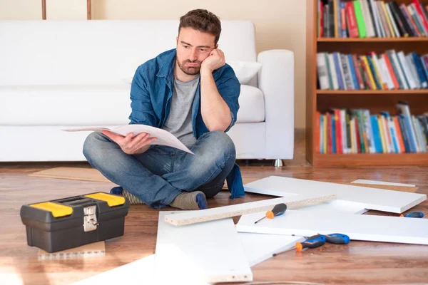 Glücklicher junger Mann beim Lesen der Anleitung zum Zusammenbau von Möbeln — Stockfoto