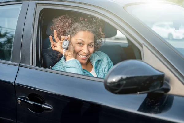 Женщина-водитель черного автомобиля улыбается, показывая ключи от новой машины и автомобиль — стоковое фото