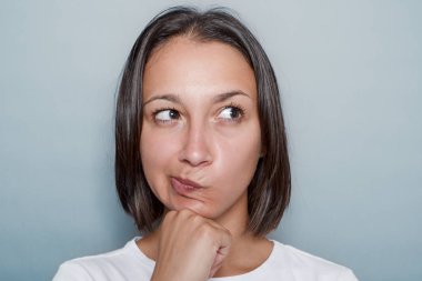 Gri arka planda yüz ifadesi düşünen kadın