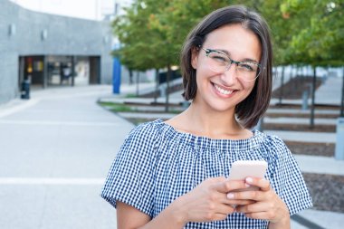Şehir caddesinde neşeli bir kadın telefonda mesajlaşıyor.