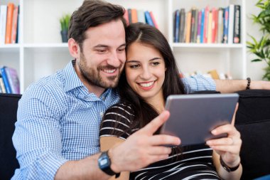 Neşeli çift, oturma kangurusunda oturmuş tablet kullanıyor.