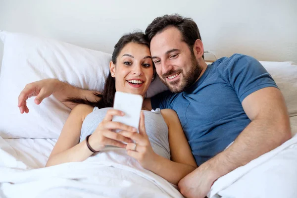 Δυο ερωτευμένοι στο κρεβάτι κρατώντας smartphone — Φωτογραφία Αρχείου