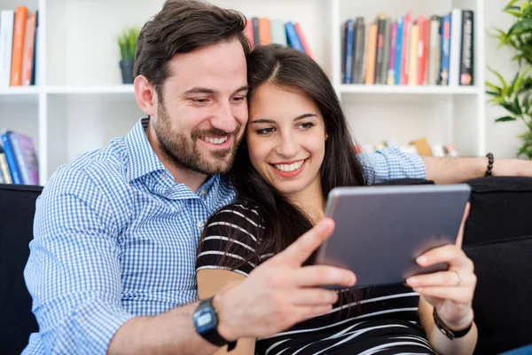 Cheerful couple using a tablet on line sitting in the living roo — Stock Photo, Image