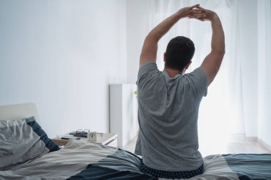 Adam sabahları yatak odasındaki yatağa kaslarını gerer.