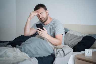 Bir adam cep telefonundan yatak haberleri okuyor.
