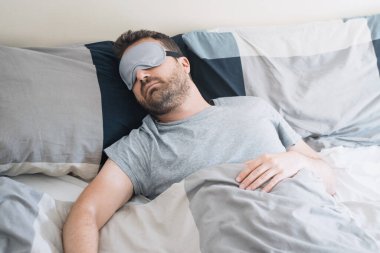 Yatakta uyuyan göz maskesi takan bir erkek portresi.