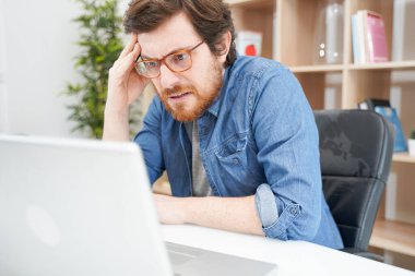 Endişeli adam ofiste oturuyor ve kredi kartı kullanıyor.