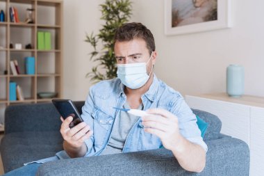 Grip belirtileri gösteren bir adam sıcaklığı ölçüyor ve doktor çağırıyor.