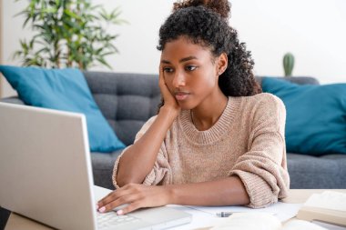 Oturma odasında dizüstü bilgisayar kullanan siyah bir kız.