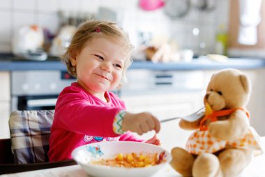 Çatal sebze ve makarna yemek bebek kız. Besleme ve oyuncak oyuncak ayı ile oynarken küçük çocuk.