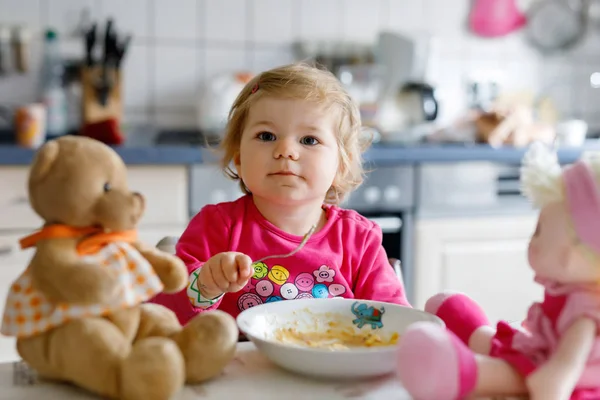 Çatal sebze ve makarna yemek bebek kız. Besleme ve oyuncak bebekle oynarken küçük çocuk — Stok fotoğraf