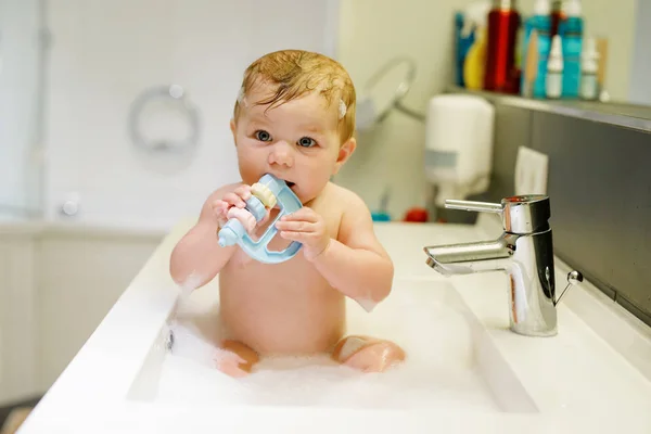 Niedliches entzückendes Baby badet in Waschbecken und spielt mit Wasser und Schaum — Stockfoto