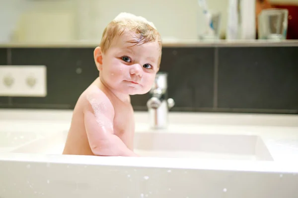 Bebê adorável bonito tomando banho na pia de lavagem e brincando com água e espuma — Fotografia de Stock