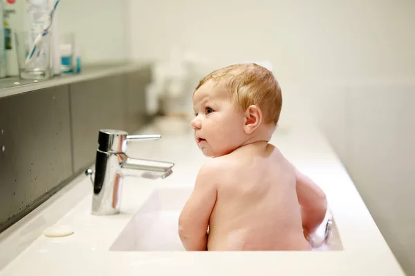 Bebê adorável bonito tomando banho na pia de lavagem e brincando com água e espuma — Fotografia de Stock