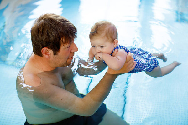 Happy middle-aged father swimming with cute adorable baby girl in swimming pool.