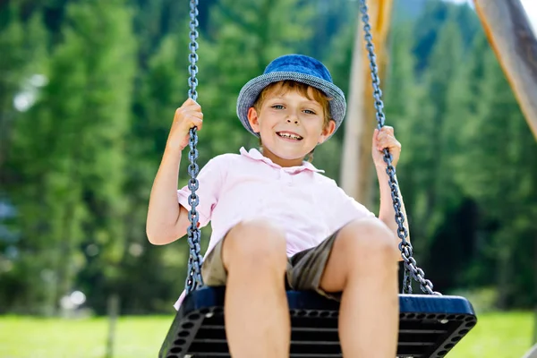 Lustiger kleiner Junge hat Spaß mit Kettenschaukel auf Spielplatz im Freien, während er nass mit Wasser bespritzt wird — Stockfoto