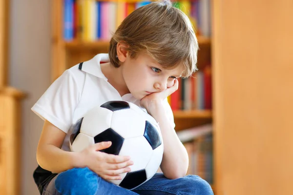 可悲而不快乐的小男孩与足球有关丢失的足球或足球比赛。在电视上看完比赛的孩子 — 图库照片