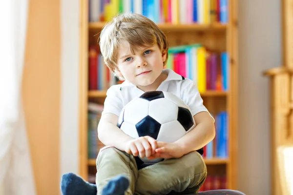 Pequeño niño rubio preescolar con bola viendo fútbol partido de la taza de fútbol en la televisión. —  Fotos de Stock