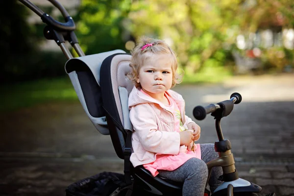 Schattig schattig peuter meisje zittend op duwen bicyle of driewieler. Klein kindje gaat wandelen met ouders op zonnige dag. — Stockfoto