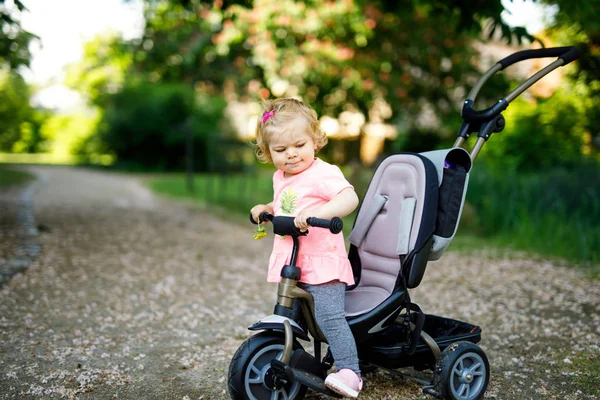 Linda niña adorable niño sentado en bicicleta empujando o triciclo. Niño pequeño que va a dar un paseo con sus padres en un día soleado. — Foto de Stock