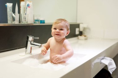 Lavaboda yıkanan, su ve köpükle oynayan sevimli bir bebek.